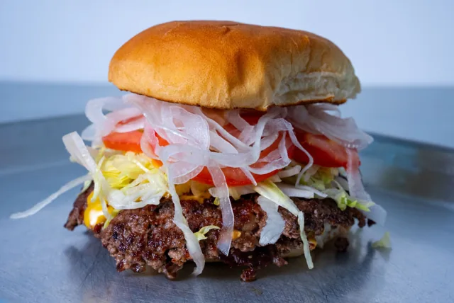 A cheeseburger topped with lettuce, tomato and fresh onion