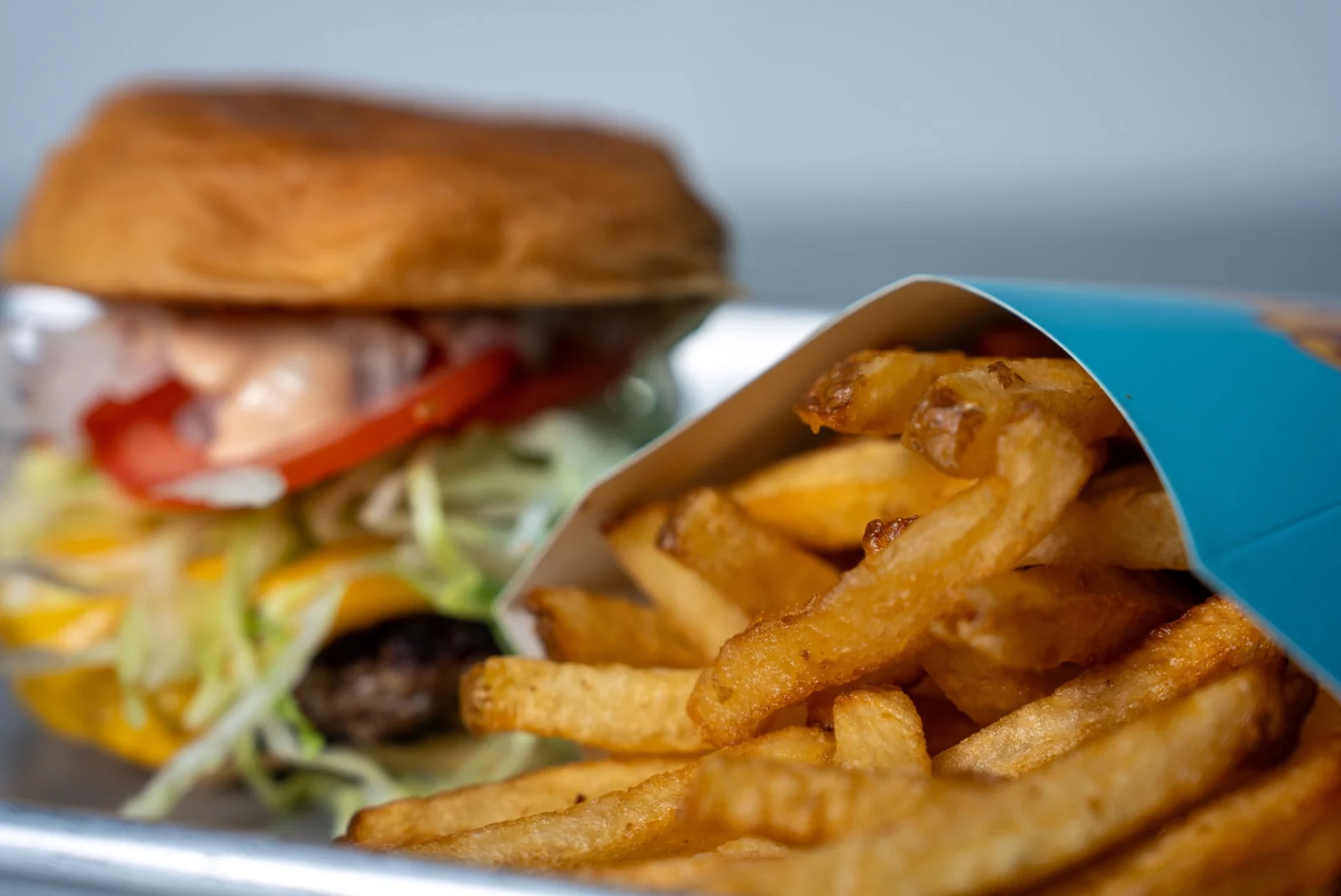 Golden hand-cut fries in a blue sleeve, with a burger softly blurred in the background