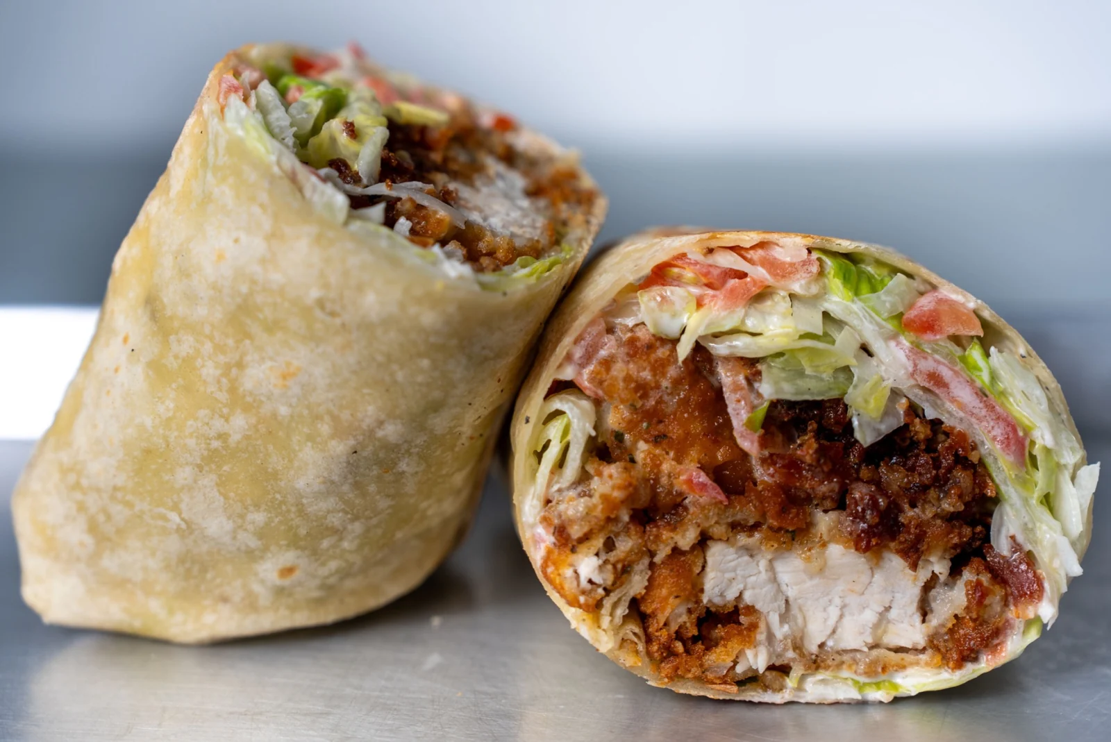 A crispy chicken wrap with tomato, bacon, lettuce and cheese, cut to show the filling