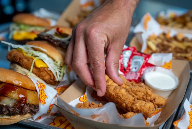 A crispy chicken tender being picked up from a tray beside dipping sauce