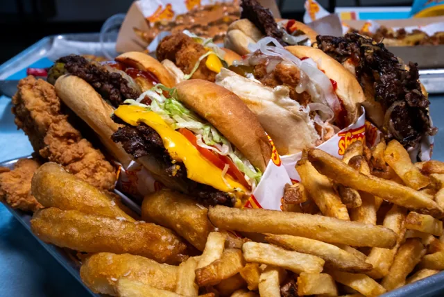 A close-up spread of beef burgers, golden fries, onion rings and chicken tenders