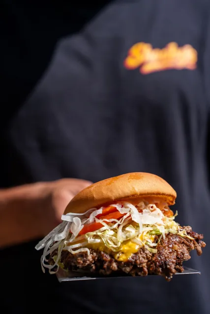 A hand-held burger with lettuce, tomato and melted cheese